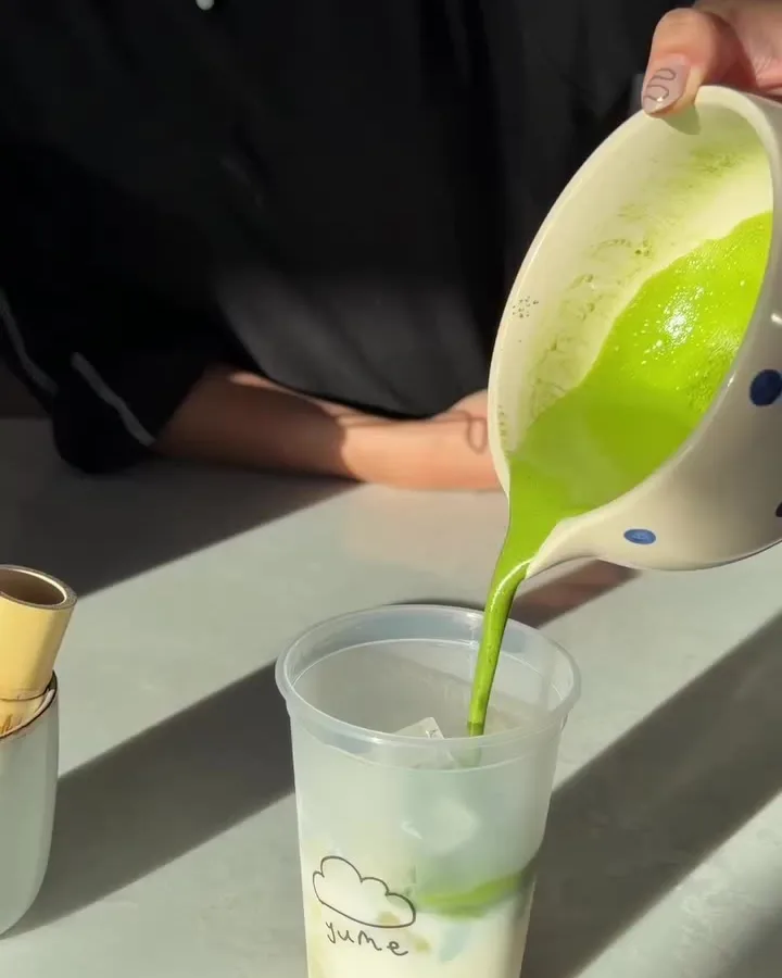 Bright green matcha being poured over a cup of milk and ice