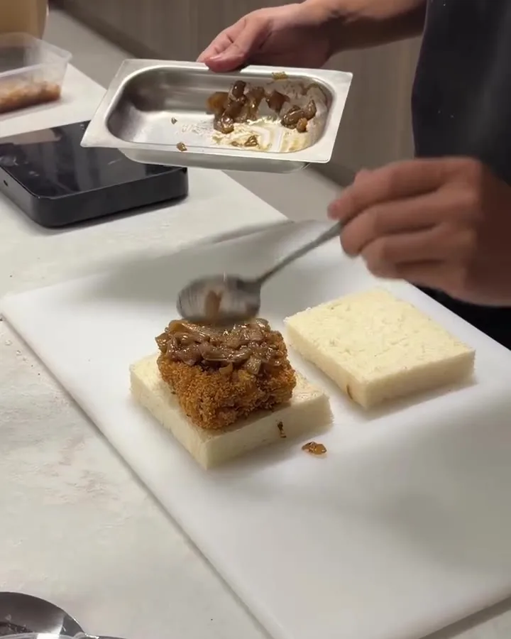 A katsu sando being built on the board, sauce spooned over the chicken